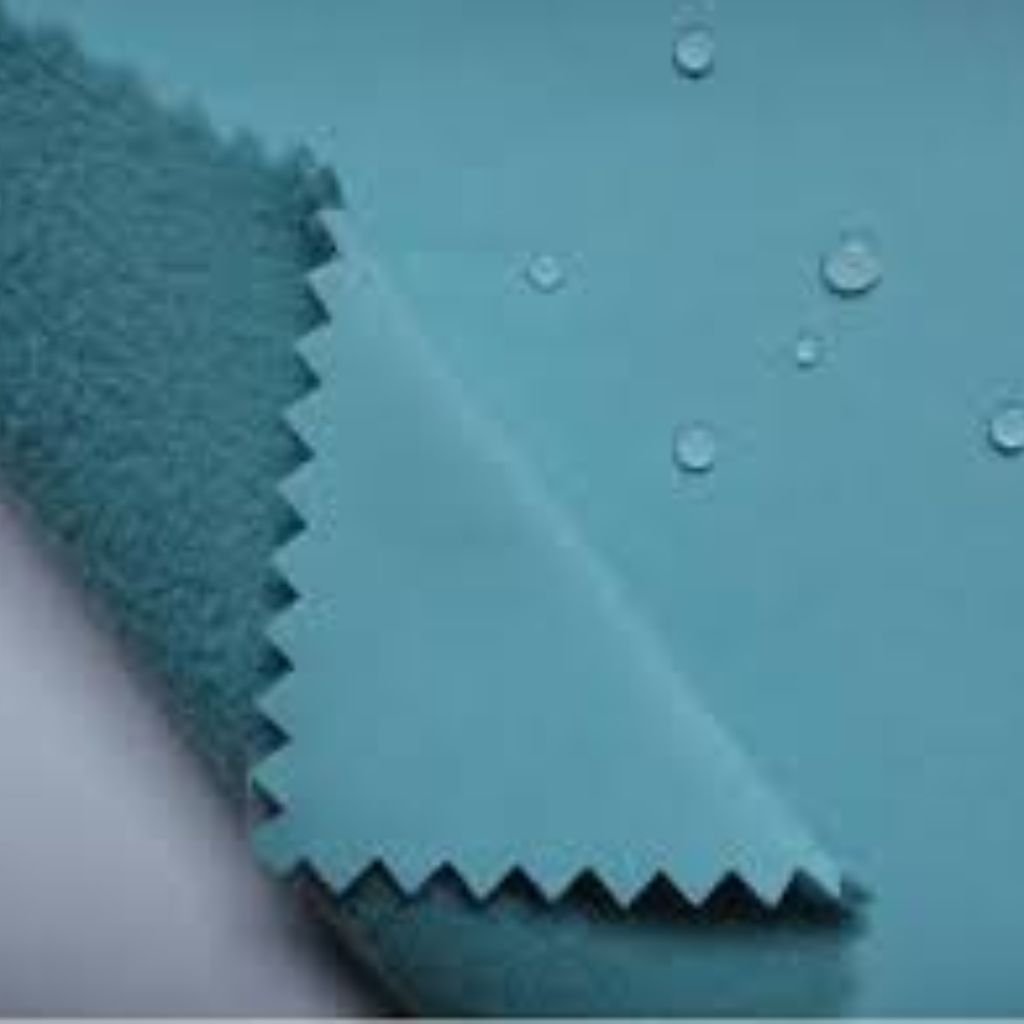 A colorful fabric with a bold fruit-and-leaf pattern, featuring yellow and orange mango-like shapes and teal leaves, with a corner of the fabric peeled back to reveal its white underside.Does Shell Fabric