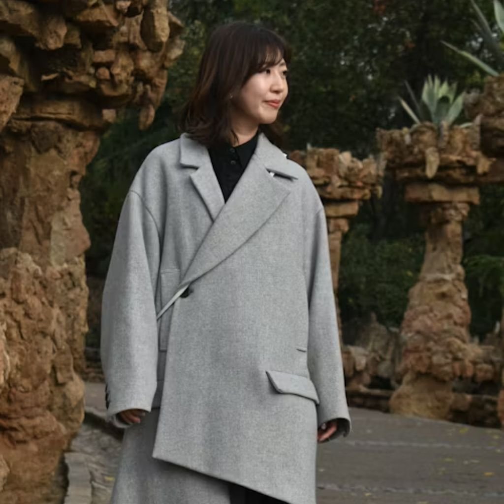 A person in side profile wearing a long dark coat, brown skirt, and flat cap against a white background.Is a Long Parka Coat Worth It?