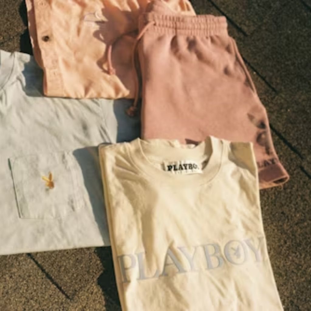 Folded casual clothing in soft pastel colors laid out on a textured surface, including T-shirts and drawstring shorts.Lambswool Clothing