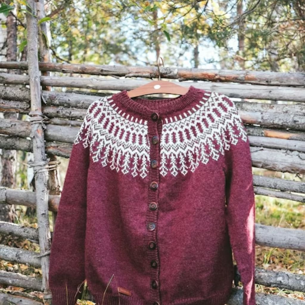 Burgundy knit cardigan with a white Nordic pattern hanging on a wooden hanger outdoors.Lambswool Clothing