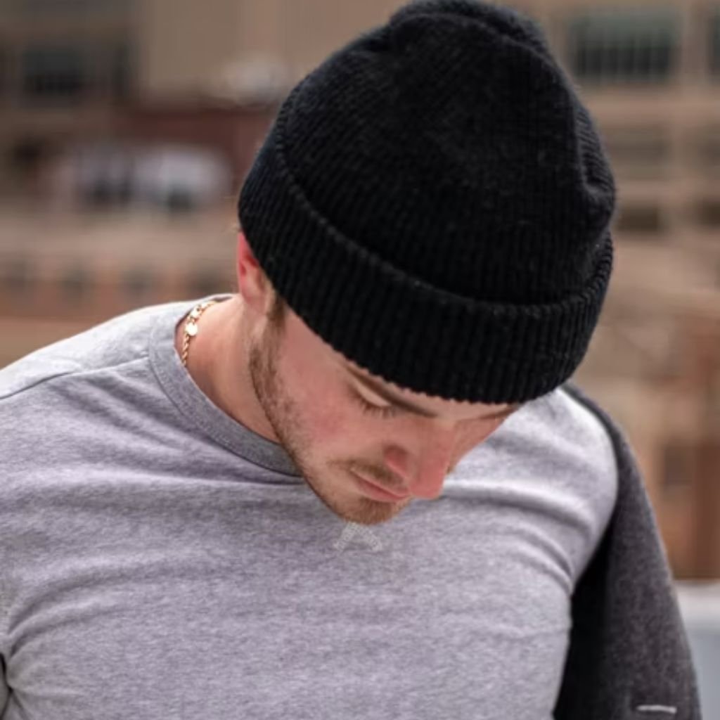 A man wearing a brown shearling-lined coat and mustard turtleneck stands outdoors, leaning against a black iron railing.The Wool Peacoat Comeback: