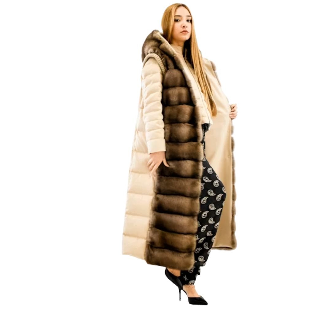 A person wearing a camel-colored belted coat stands with hands in pockets against a stone wall.Is a Long Parka Coat Worth It?