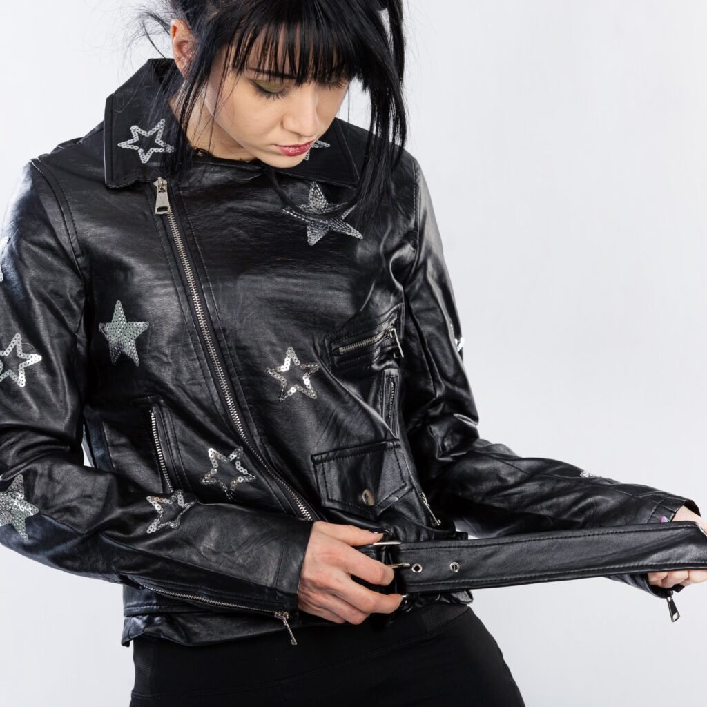 A person wearing a black leather jacket with silver star patches, looking down as they adjust the belt at the waist.