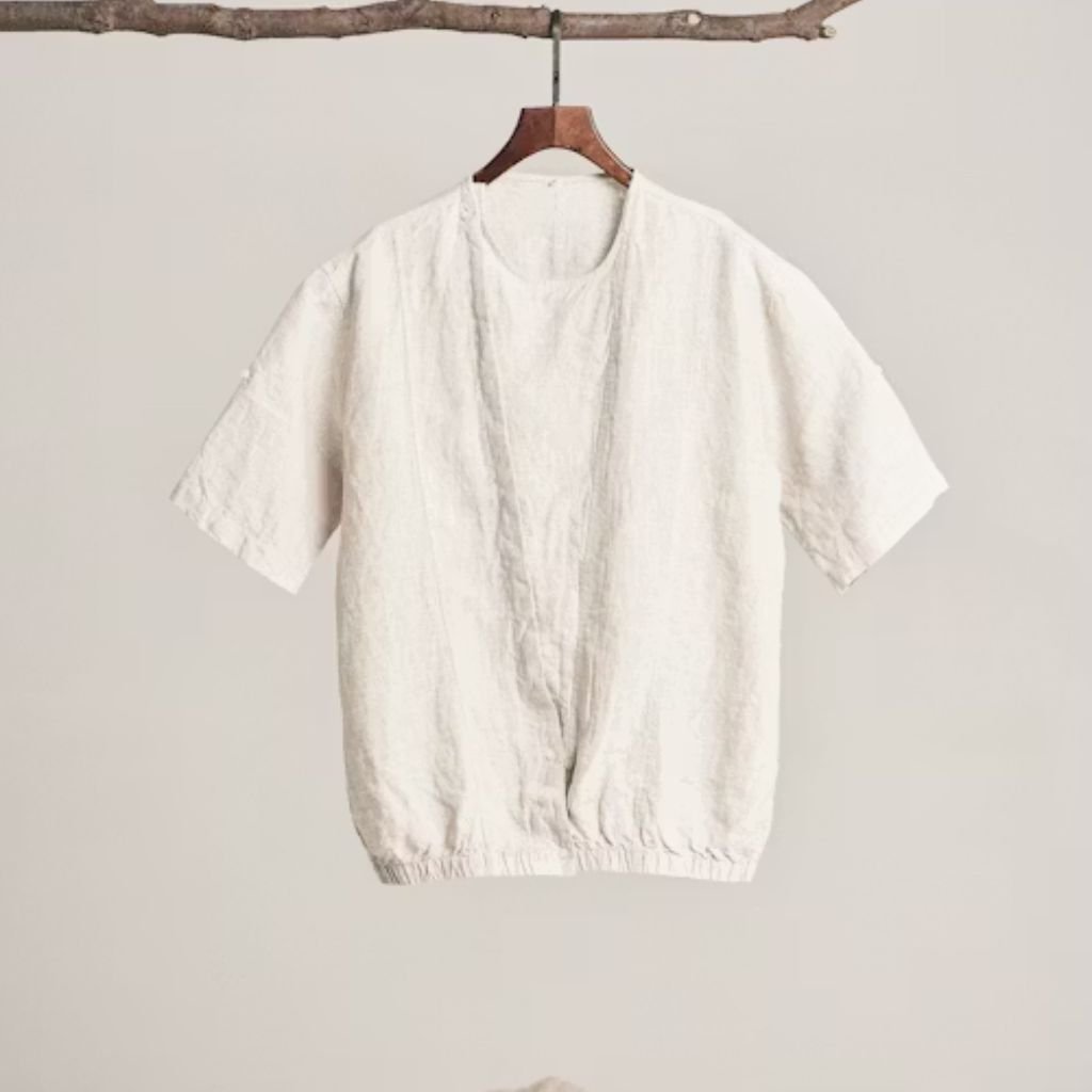 Off-white short-sleeve linen blouse hanging on a wooden hanger against a neutral background.Lambswool Clothing