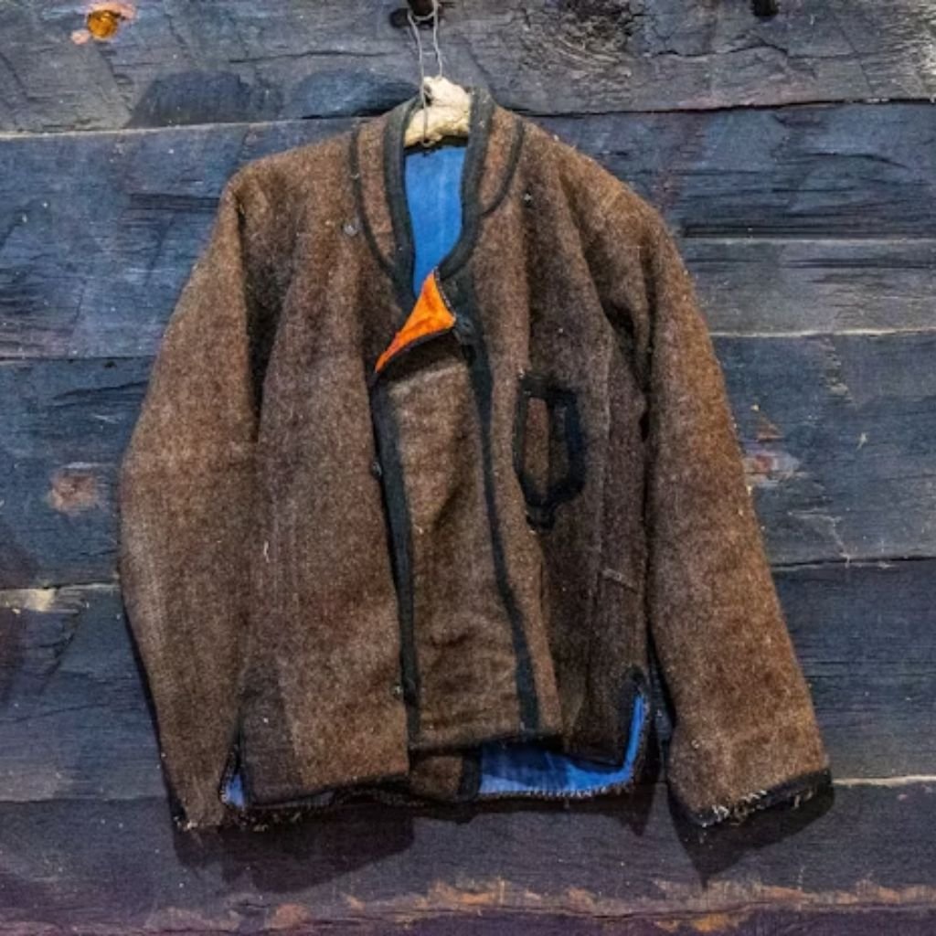 Person wearing a black coat with a light shearling collar, standing outdoors in a rocky setting.The Wool Peacoat Comeback: