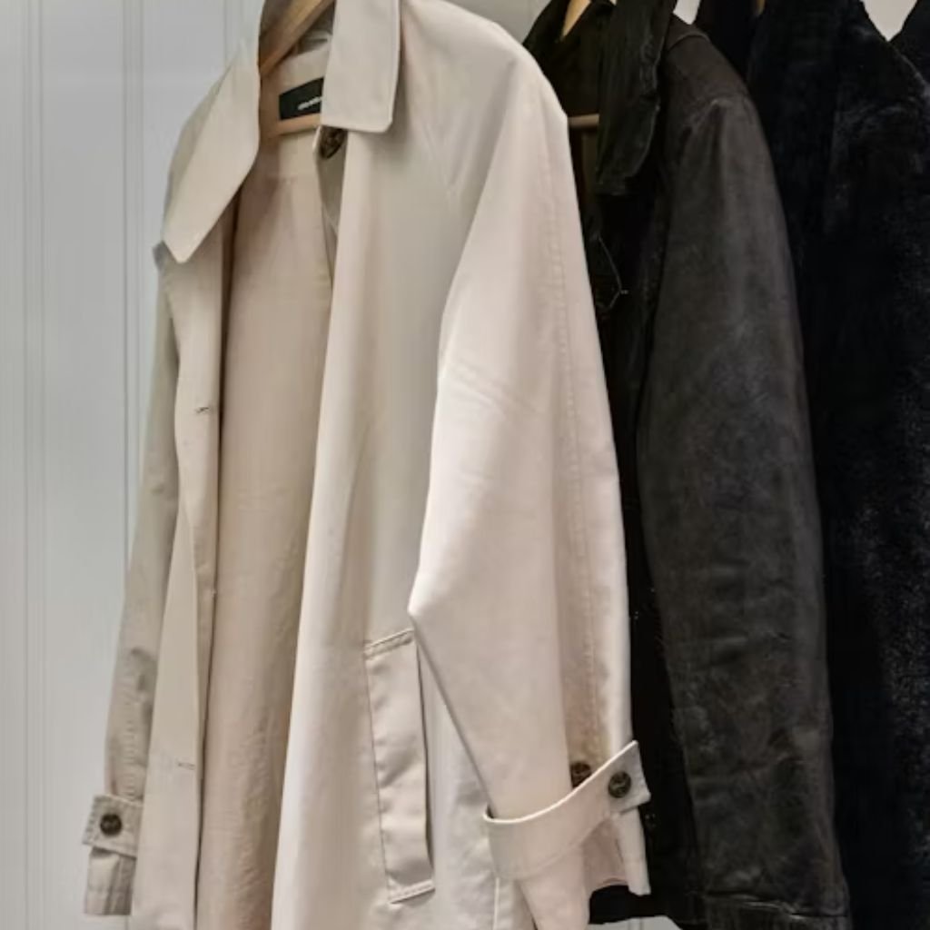 A person wearing a black baseball cap, black sleeveless top, and a black puffer jacket draped off one shoulder stands against a light-colored wall.Belted Winter Coats