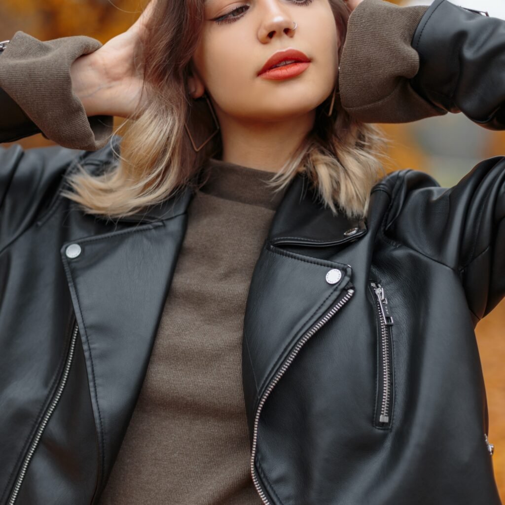 A close-up of a person wearing a black zip-up leather jacket with silver zippers, brown knit cuffs, and a brown top underneath.
