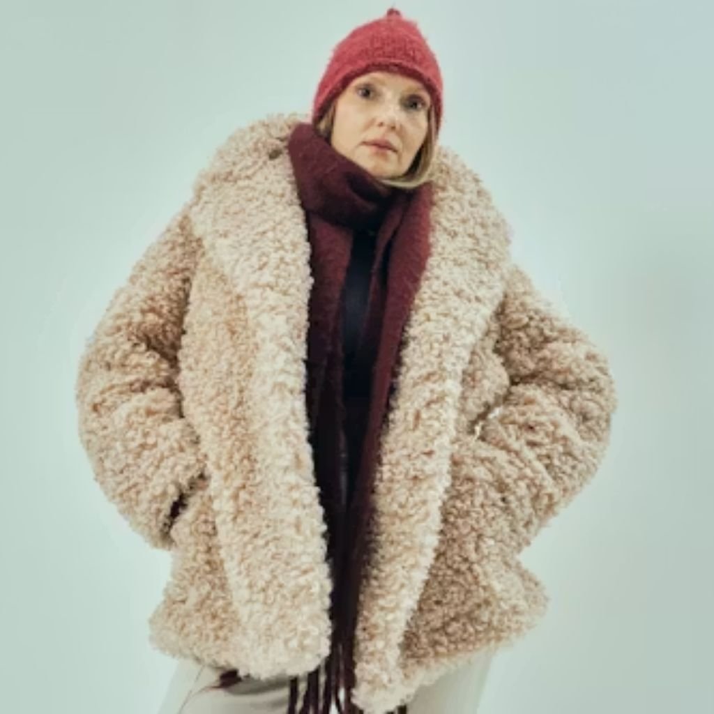 A person wearing leopard-print sunglasses and a brown faux-fur jacket, looking to the side against a light-colored wall.The Wool Peacoat Comeback: