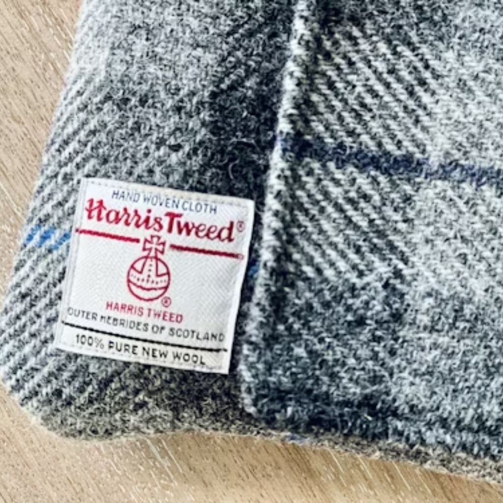 The image shows a close-up view of a dark, four-hole button attached to a gray fabric garment. The textured weave of the fabric is clearly visible, and a faint seam line runs diagonally across the frame. Another button appears softly out of focus in the background, creating depth and emphasizing the craftsmanship and material quality of the garment.Does Shetland Wool Itch?