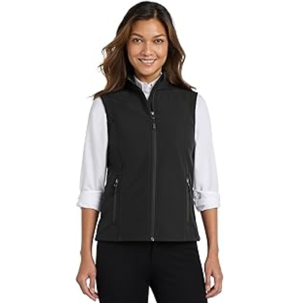 A woman wearing a black zip-up vest over a white long-sleeve shirt, smiling and standing against a plain white background.Does Shell Fabric