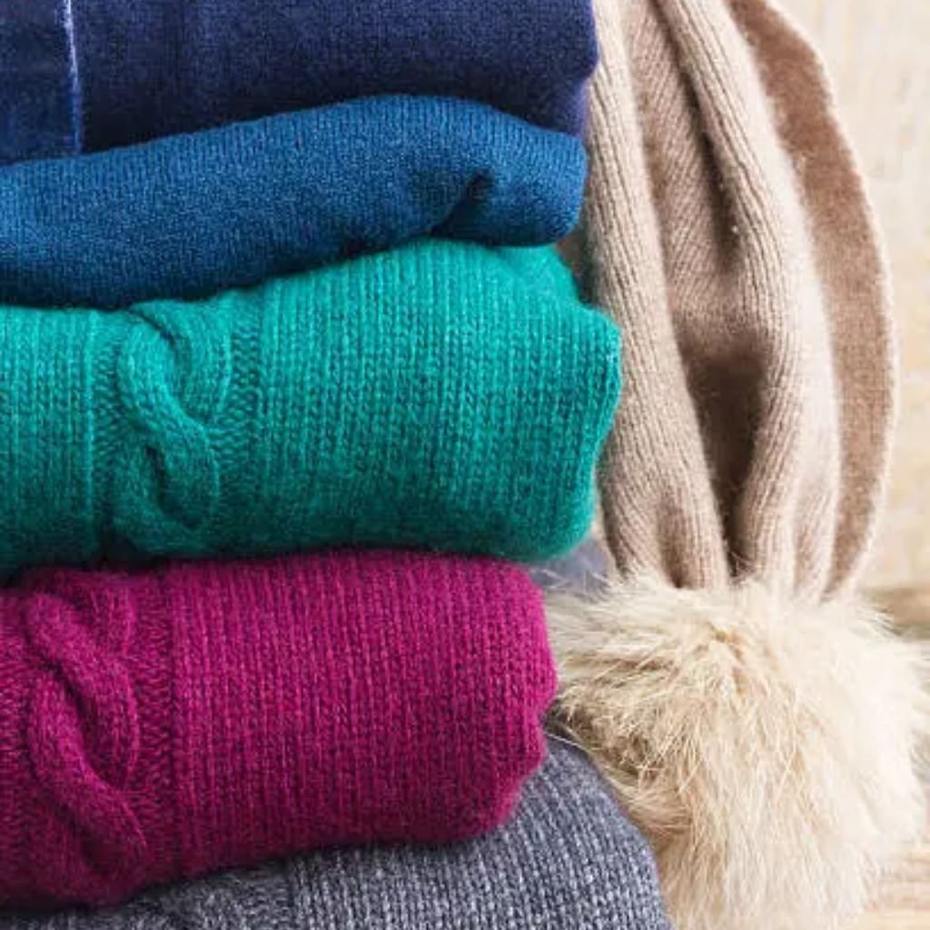 Stack of folded colorful wool sweaters in teal, navy, magenta, and grey tones with a soft knit texture.Lambswool Clothing