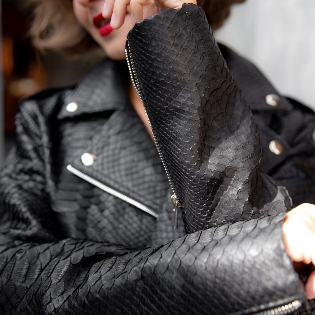 "Close-up of a black leather fashion jacket with a textured snakeskin pattern, metal zippers, and silver buttons."
