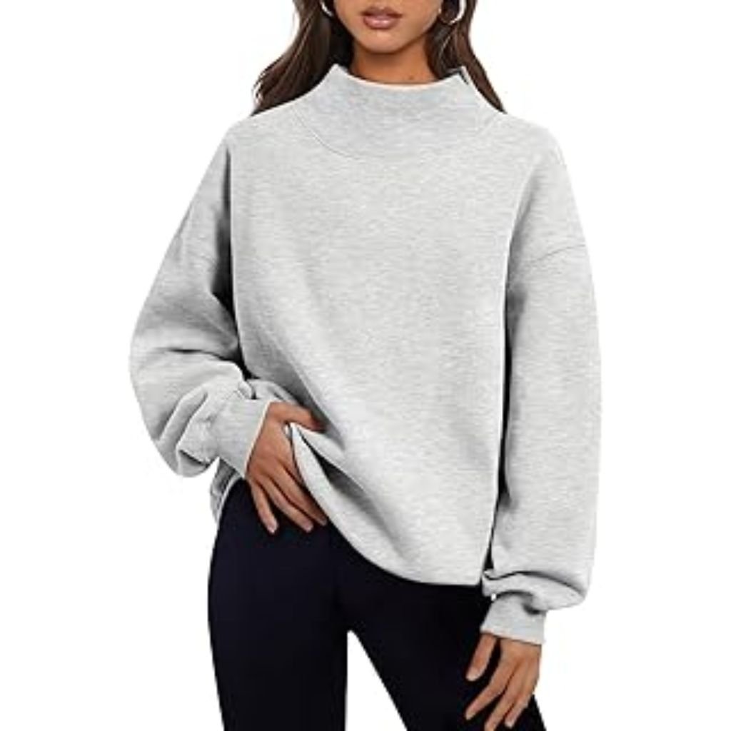 A woman wearing a light gray oversized mock-neck sweatshirt paired with black pants, posing with one hand tucked into the hem of the sweatshirt.Why Mock neck turtlenecks