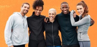 What Is Track Jacket A Complete Guide to This Sporty Classic A diverse group of five friends stands arm-in-arm against an orange wall, smiling at the camera. They’re dressed in athletic wear. What Is Track Jacket