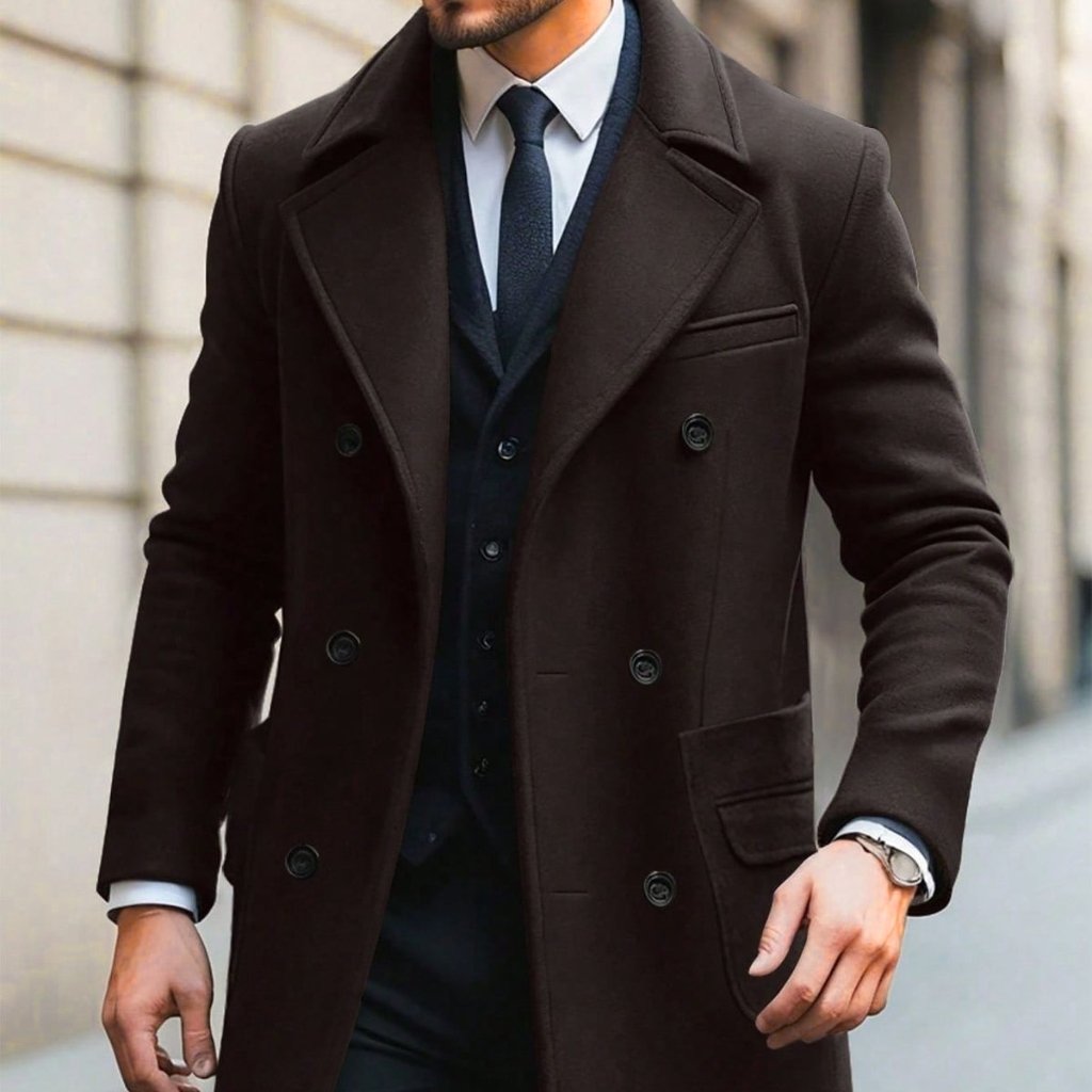 A man wearing a stylish dark brown double-breasted overcoat over a navy suit and white dress shirt, walking outdoors in an urban setting.