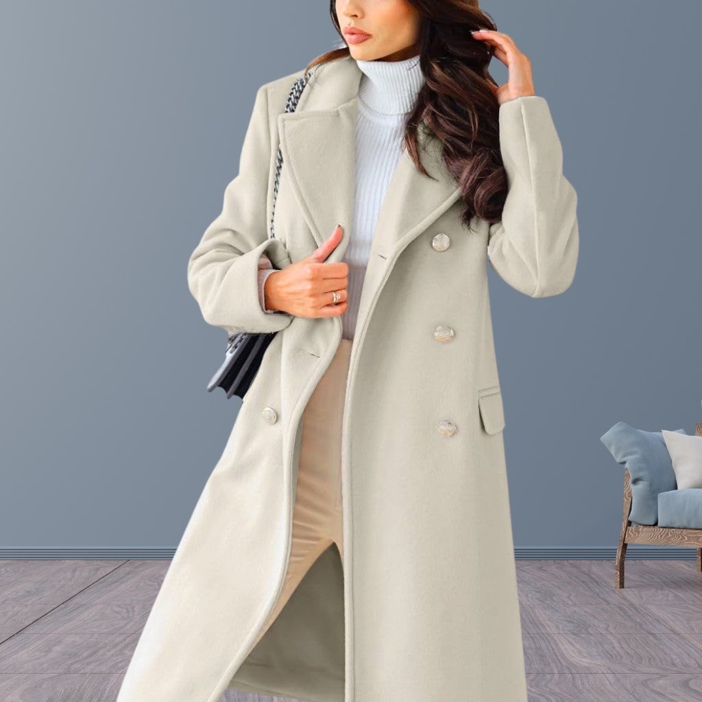 A stylish woman wearing a long, light beige wool coat over a white turtleneck sweater and beige pants. She carries a black handbag with a chain strap and poses with one hand adjusting her hair.