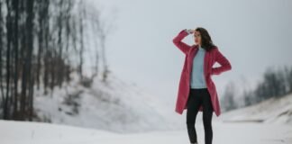 Winter Fleece Topcoat Guide: Comfort, Style, and Durability A woman stands in a snowy landscape wearing a pink coat, light blue sweater, black pants, and beige boots, shielding her eyes from the light with one hand. Winter-Fleece Topcoat