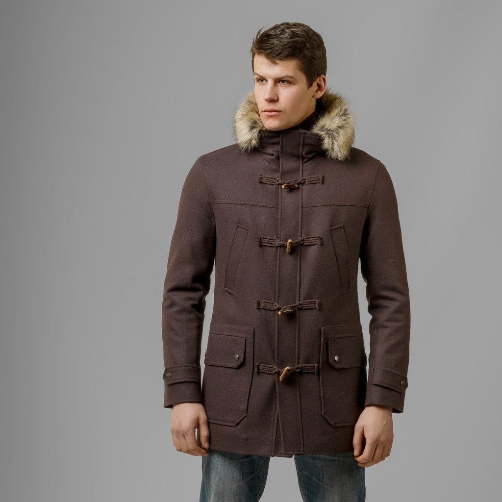 A man wearing a dark brown wool parka with a fur-trimmed hood and toggle closures, standing against a gray background.