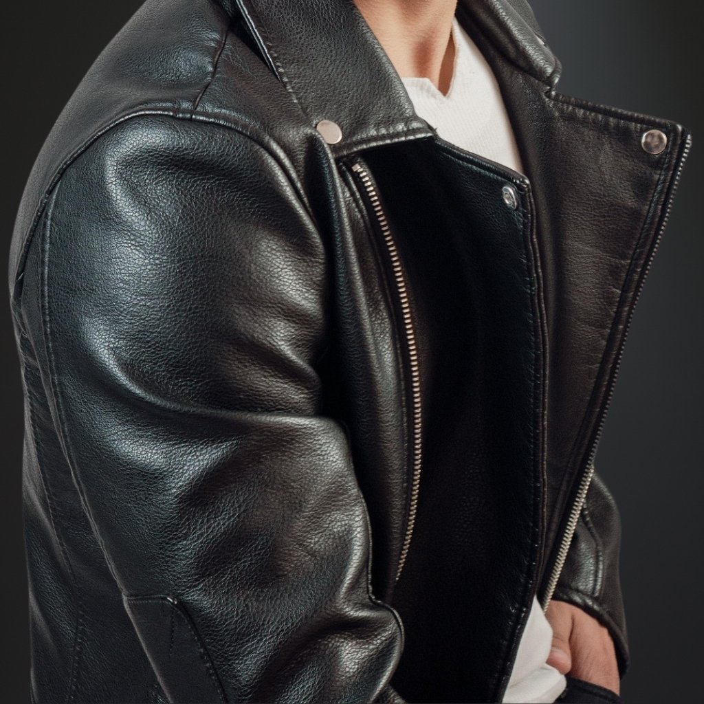  A man wearing a black leather parka jacket with a silver zipper, standing with one hand in his pocket.