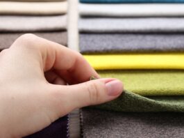 A close-up of a hand lifting a green fabric swatch from a stacked array of colorful cloth samples.