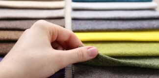 Blended Cashmere Wool Fabric Guide for Soft, Durable Fashion A close-up of a hand lifting a green fabric swatch from a stacked array of colorful cloth samples.