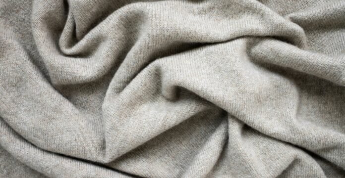 Soft beige cashmere wool fabric with a smooth knitted texture, gently draped to highlight its fine weave and natural warmth.