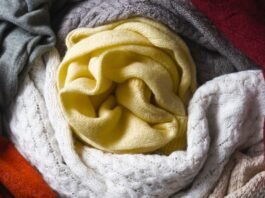 Combed Grade A Cashmere Wool Fabric A colorful assortment of knitted scarves arranged in a circular coil, featuring yellow, white, gray, orange, and burgundy tones.