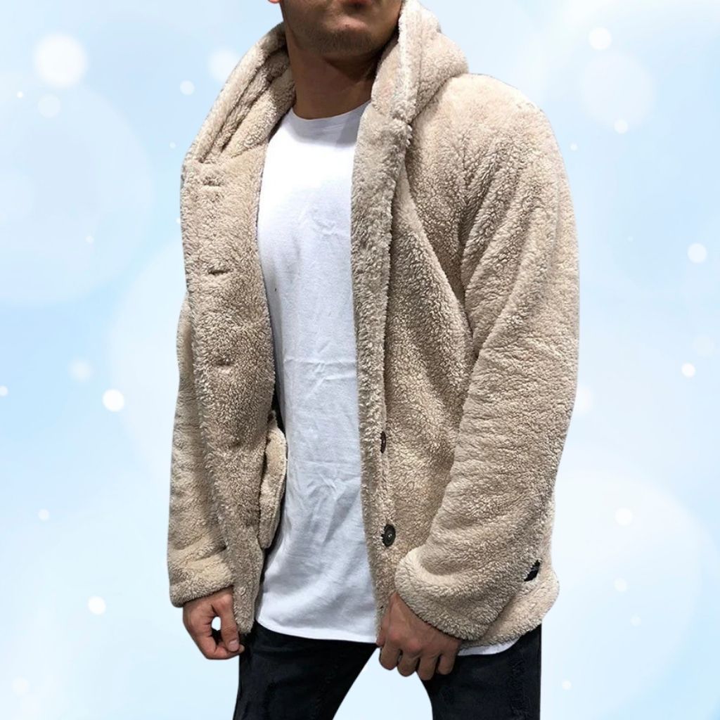 A person wearing a cozy beige plush jacket over a white t‑shirt, standing against a soft blue background.