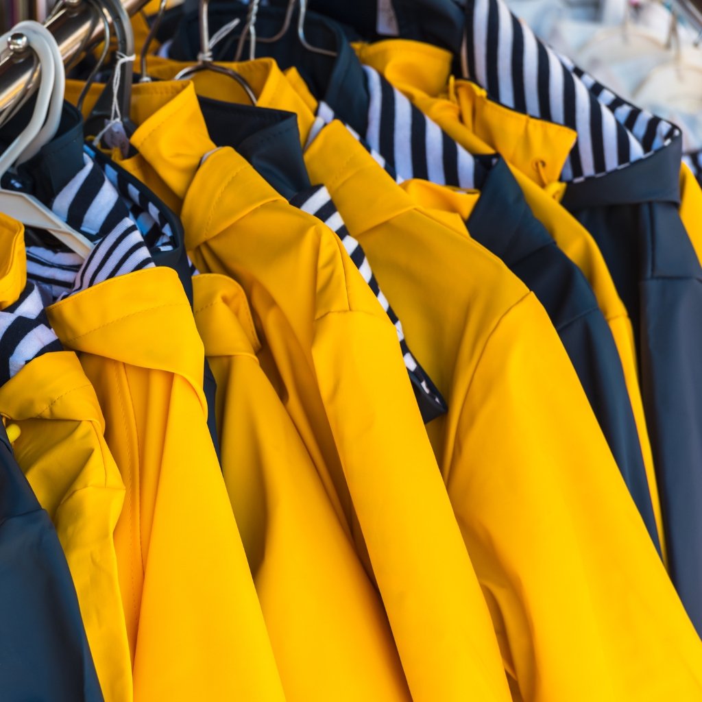  A row of bright yellow and navy rain jackets hanging on hangers with striped blue-and-white linings visible.