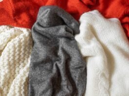 Grade A Pashmina Cashmere A close-up of folded knit fabrics in cream, gray, white, and red tones with a peach scarf draped over.