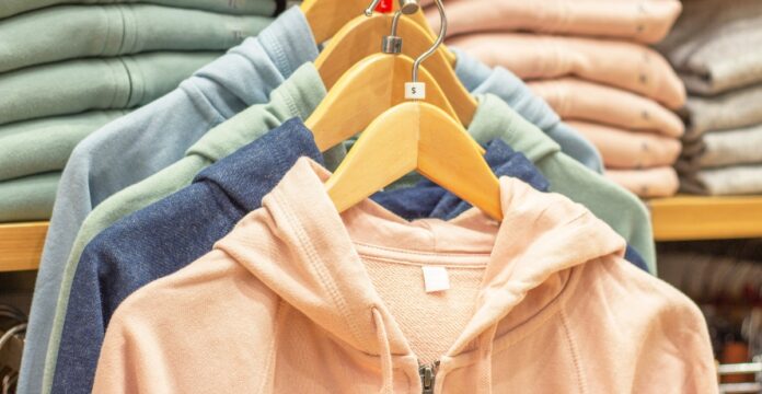 A rack of pastel-colored hoodies on wooden hangers in a store, with soft beige, pink, blue, and green jackets.