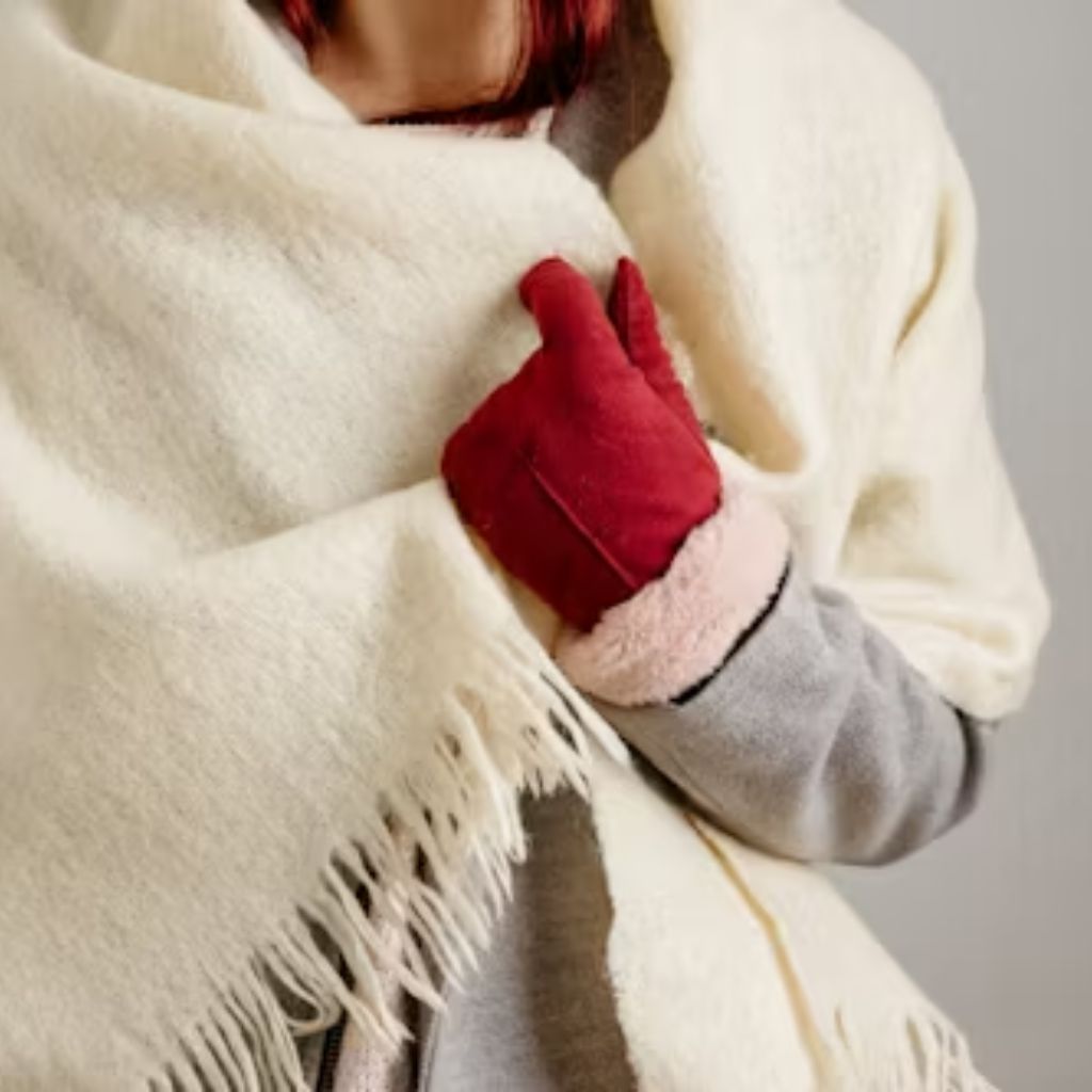 Soft Winter Fabrics for Sensitive Skin: Cozy & Itch-Free Now 9 A person wearing a white fringed shawl and a red mitten, with a gray sleeve visible, hugging the shawl close to their chest.
Soft Winter Fabrics for Sensitive Skin: