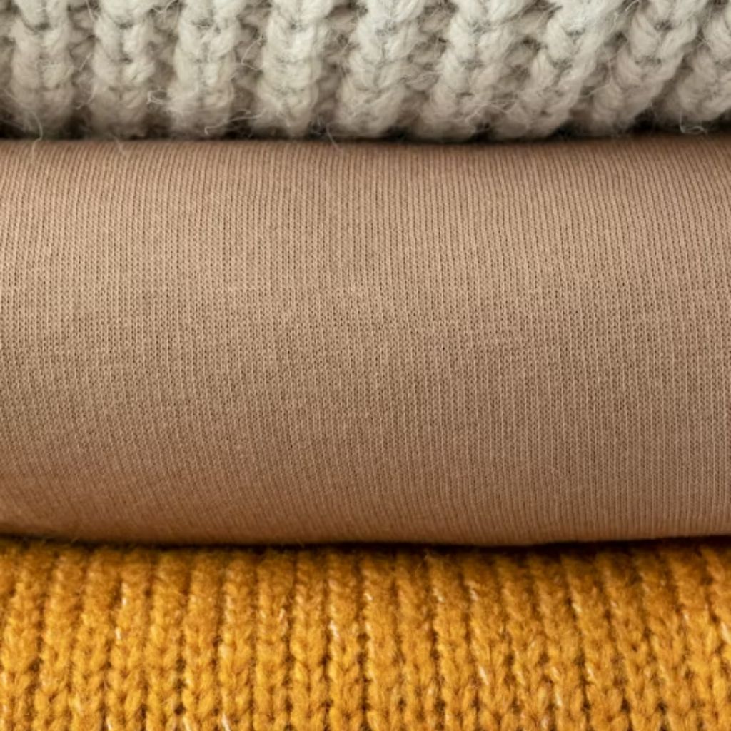 Alt text: “Stack of three folded fabrics: top appears as a chunky knit in light gray, middle is smooth camel/beige knit, bottom is mustard yellow ribbed knit.”

Vegan Winter Fabric Explained: