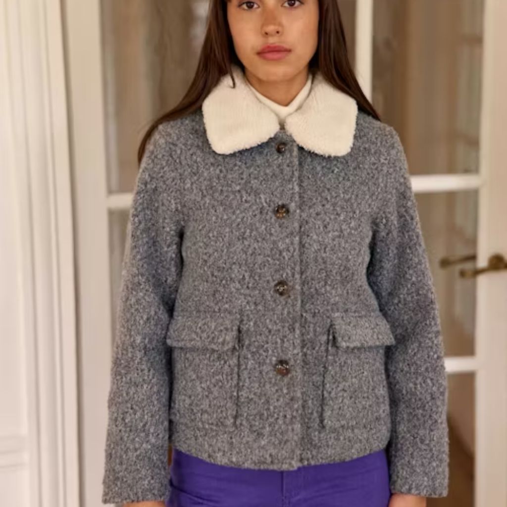 A young woman indoors wearing a gray tweed jacket with a large white faux-fur collar, a white turtleneck, and purple pants. The jacket features three brown buttons and two waist pockets.

Cozy Casual Winter Jacket: