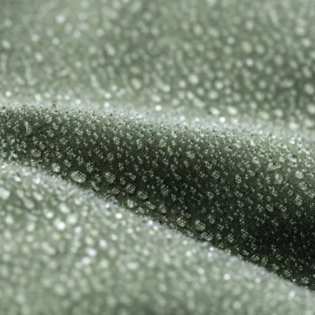 Macro close-up of dark green fabric with numerous white speckles or droplets scattered across the surface.

Moisture-Wicking Winter Fabric Explained:
