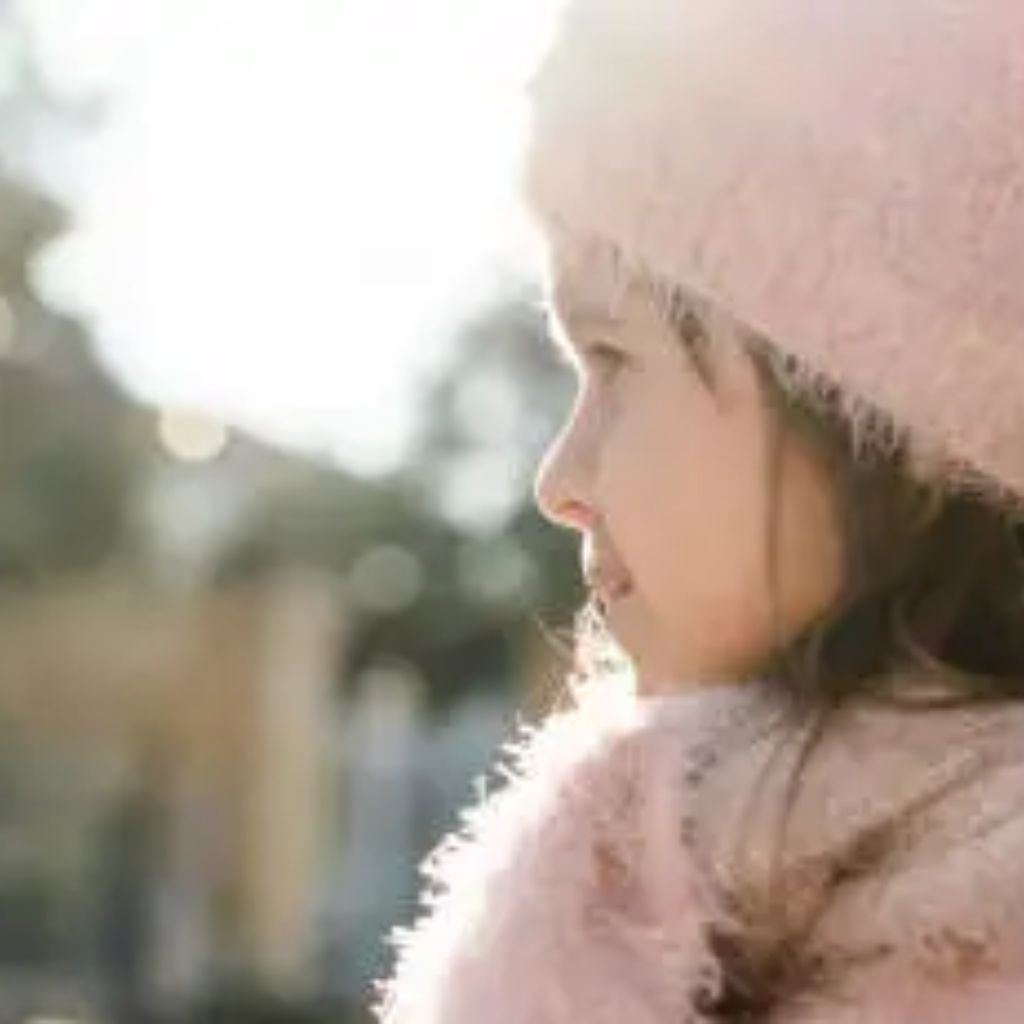 Sustainable Wool Winter Coat: Warmth with a Green Touch Eco 10 Alt text: A close-up side profile of a young woman wearing a soft pink knit beanie and a light pink scarf. The background is softly blurred, suggesting an outdoor setting with warm sunlight.
Sustainable Wool Winter Coat: