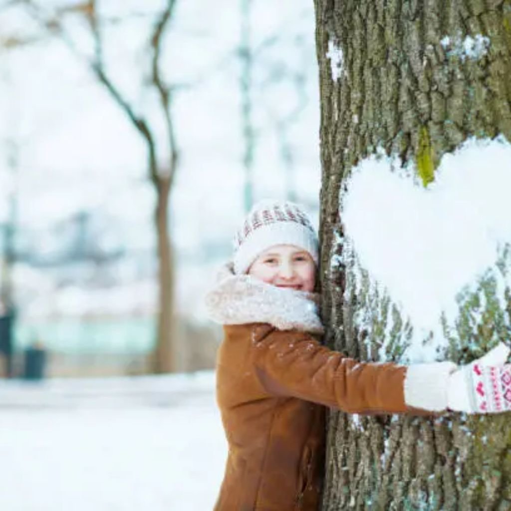 Sustainable Wool Winter Coat: Warmth with a Green Touch Eco 7 Alt text: A young girl wearing a brown winter coat, white knit hat, and white mittens hugs a snow-dusted tree in a snowy park. A heart shape is drawn in the snow on the tree trunk.
Sustainable Wool Winter Coat: