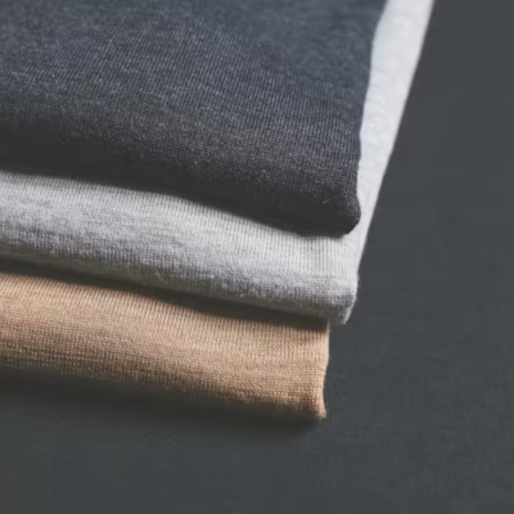 Alt text: “Close-up of three folded knitted fabrics in dark navy, light gray, and beige stacked on top of each other.”
Vegan Winter Fabric Explained: