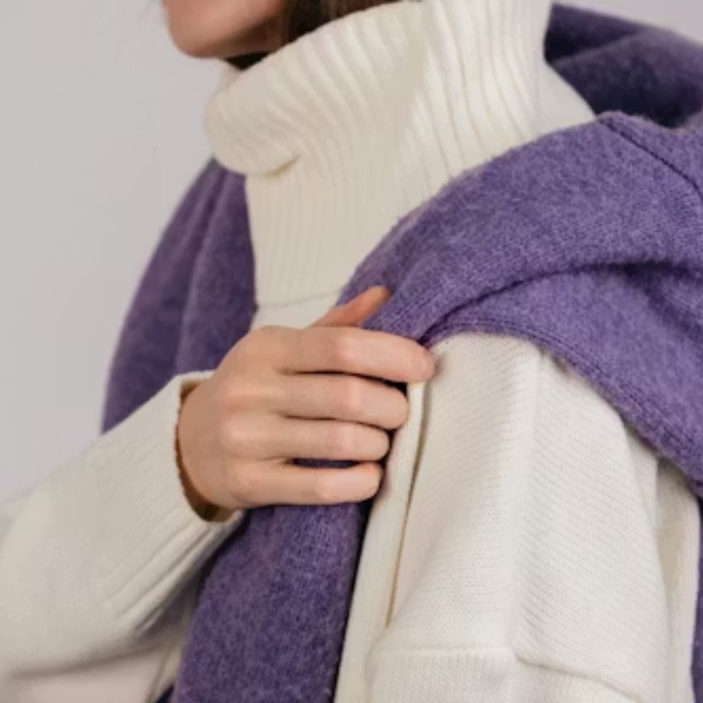 Soft Winter Fabrics for Sensitive Skin: Cozy & Itch-Free Now 12 A person wearing a white turtleneck sweater with a purple scarf draped over their shoulders, holding the scarf at the front.
Soft Winter Fabrics for Sensitive Skin: