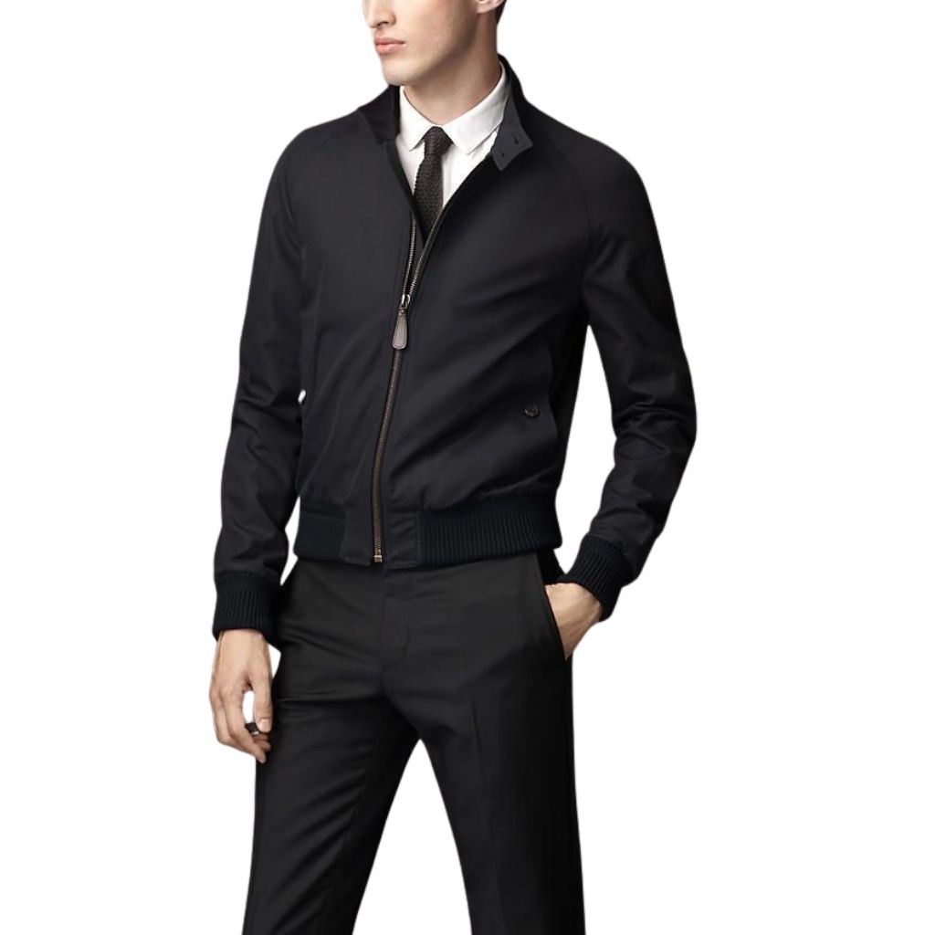 A man wearing a sleek black office jacket with a front zipper, white shirt, and tie, standing with one hand in his pocket.