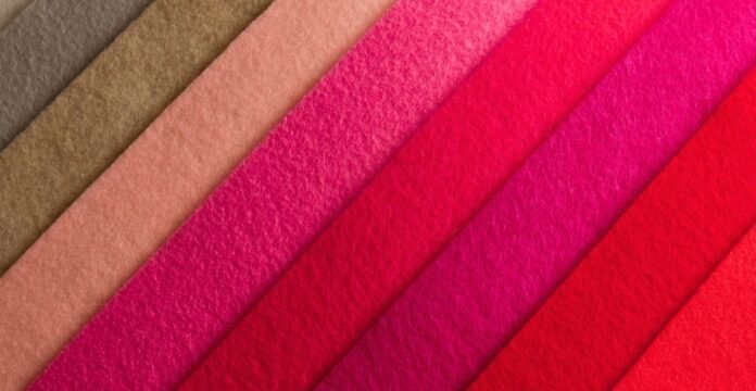 A diagonal arrangement of overlapping colorful felt strips in shades of brown, peach, pink, magenta, and red.