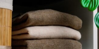 Recycled Cashmere Wool Fabric for Sustainable Clothing Recycled Cashmere Wool Fabric A stack of folded sweaters in neutral colors (brown, beige, and cream) sits on a shelf, with a wooden basket and a green plant visible on the sides.Recycled Cashmere Wool Fabric