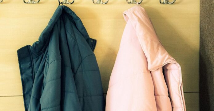 Two winter jackets hanging on hooks, one dark teal and one light pink, on a light-colored wooden wall.Minimalist Winter Jackets: