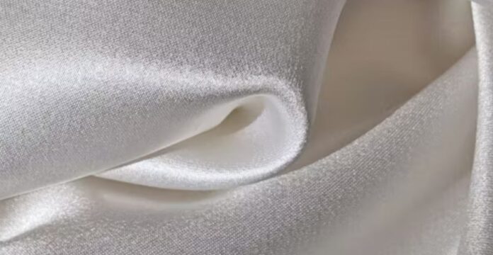 Close-up of smooth, shiny, white satin fabric with soft folds and sheen. Windproof Winter Fabric Material Guide: