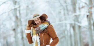 Sustainable Wool Winter Coat: Warmth with a Green Touch Eco Alt text: A smiling woman in a brown hat, brown jacket, and a colorful scarf stands in a snowy forest with snow-covered trees in the background. Sustainable Wool Winter Coat: