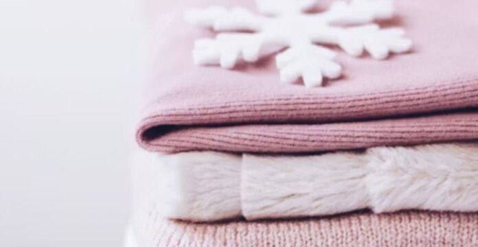 Close-up of cozy winter textiles: stacked folded fabrics in soft pink tones with a fluffy white blanket or scarf on top, creating a warm, seasonal feel. Warmest Fabrics for Winter Clothing: