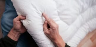 Quilted Fabric Explained: Types, Uses, Benefits & Care Guide Close-up of a person’s hands adjusting or folding a white quilted comforter on a bed.Quilted Fabric Explained: