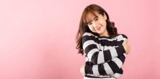 Best Winter Fabric for Extreme Cold: Heat Trapping Materials A woman with shoulder-length hair wearing a black-and-white striped sweater stands against a pink background, smiling with her arms crossed.Best Winter Fabric for Extreme Cold: