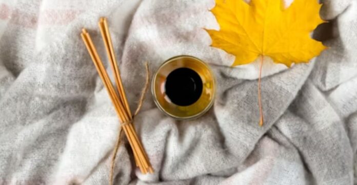 A cozy flat lay: a cup of coffee, a few cinnamon sticks tied together, and a yellow autumn leaf placed on a soft gray blanket.Soft Winter Fabrics for Sensitive Skin: