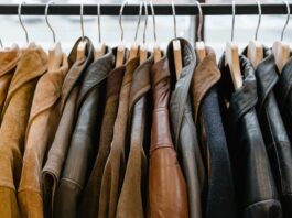 A dense row of leather and suede jackets on a clothing rack, hung on wooden hangers from a black rod. The jackets come in a range of brown and black tones, with subtle textures and stitching visible. The soft lighting highlights the materials, giving a premium, sporty-yet-sophisticated retail vibe. This image features a curated lineup of jackets in earthy browns and blacks, emphasizing varied textures like smooth leather and soft suede. The close packing and warm lighting create a tactile, sporty retail atmosphere, suggesting a premium sportswear or casual outerwear collection. Sports Jackets